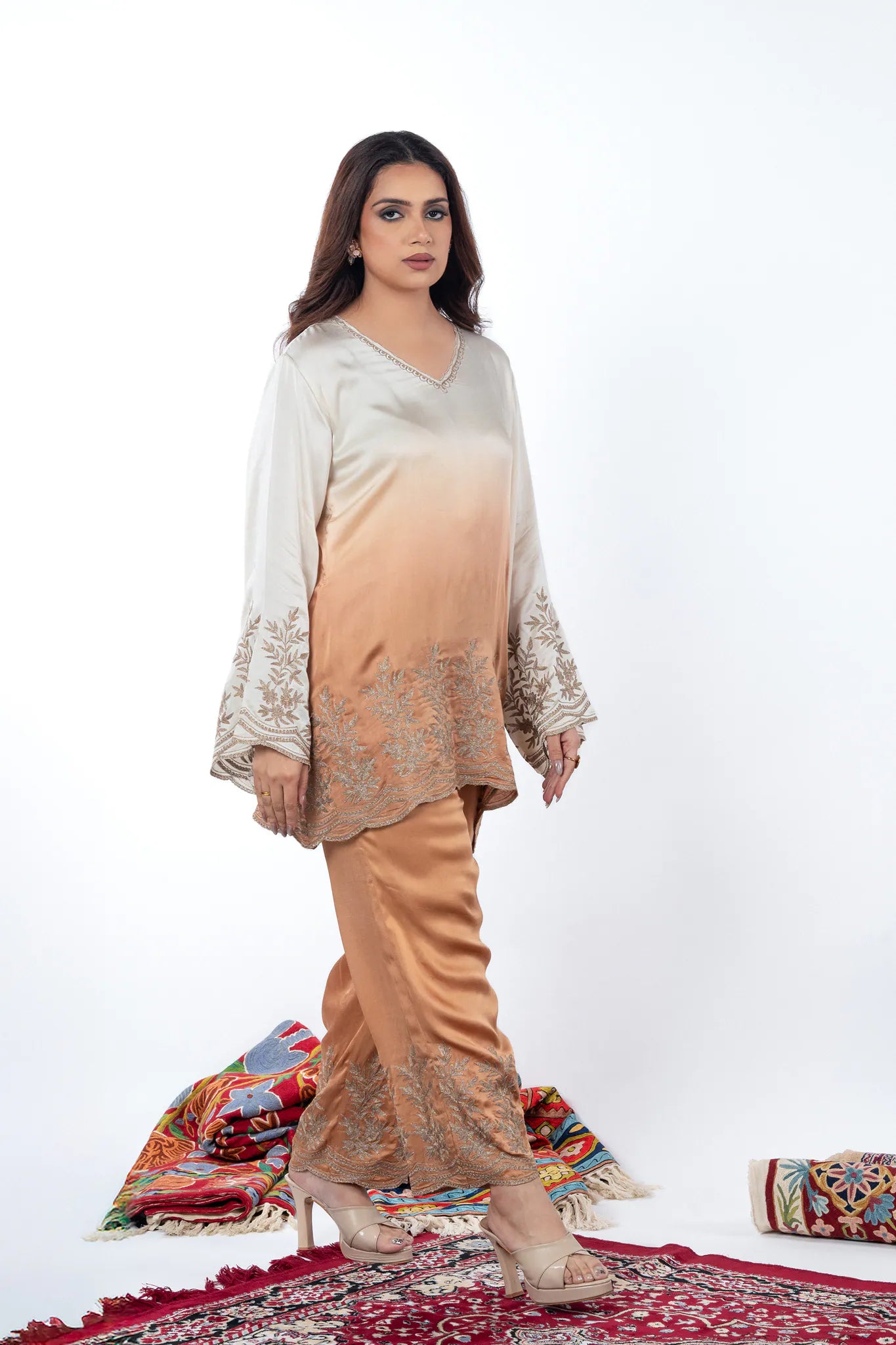 Woman wearing a traditional outfit with a white and beige top and beige pants on a white background.